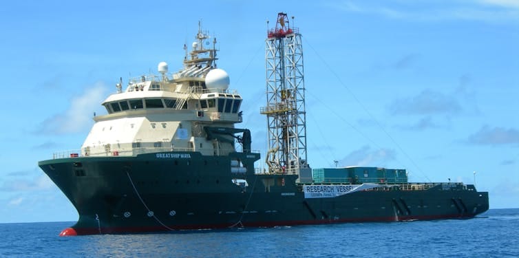 A ship with a large drill on its deck in the middle of the ocean.